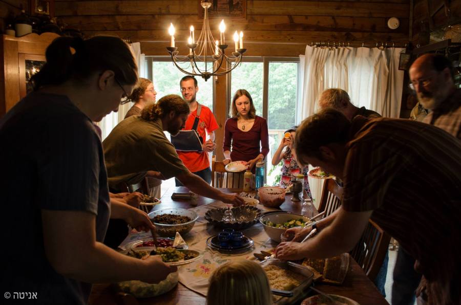 People gathered in a home standing around a table reaching for food to fill their plates